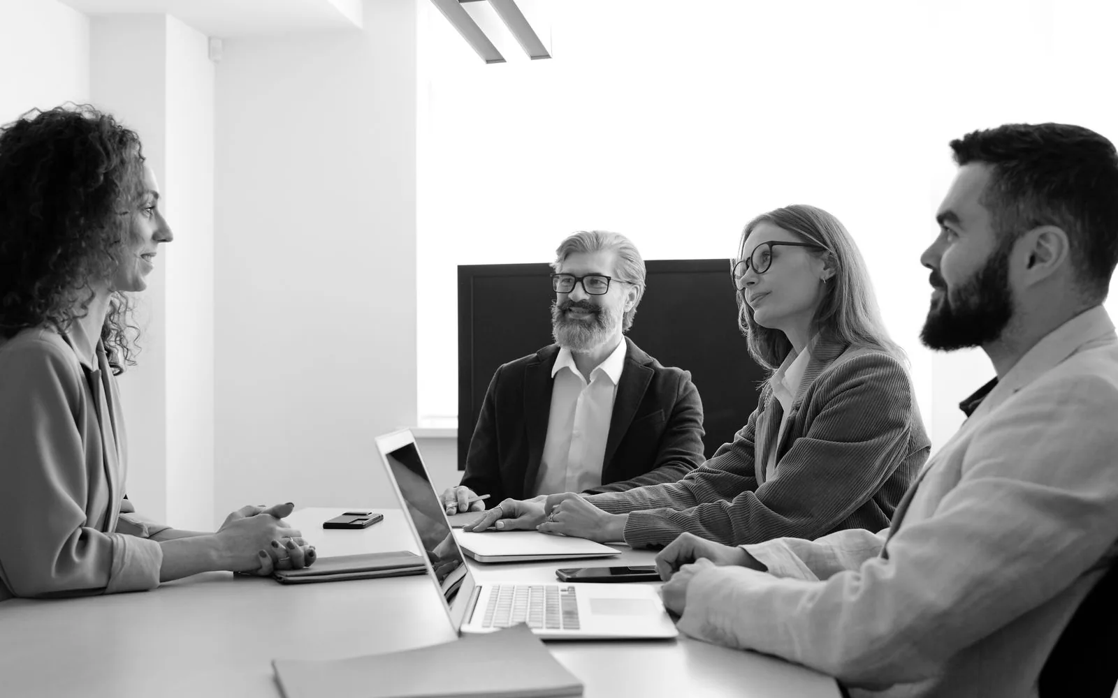Four colleagues in a meeting at a boardroom table, in black and white