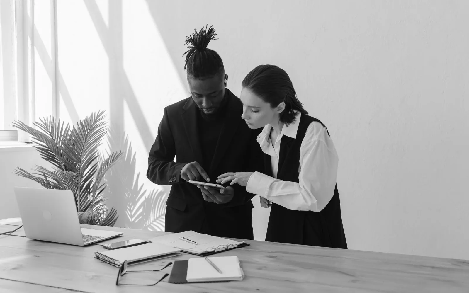 Two colleagues reading a tablet by a white wall, in black and white